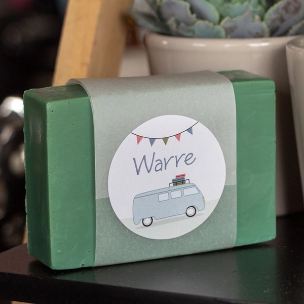 Een zeepje met een gepersonaliseerde sticker in dezelfde stijl als het geboortekaartje van Warre. Er staat de naam Warre op en de illustratie van de camper met vlaggenlijn.