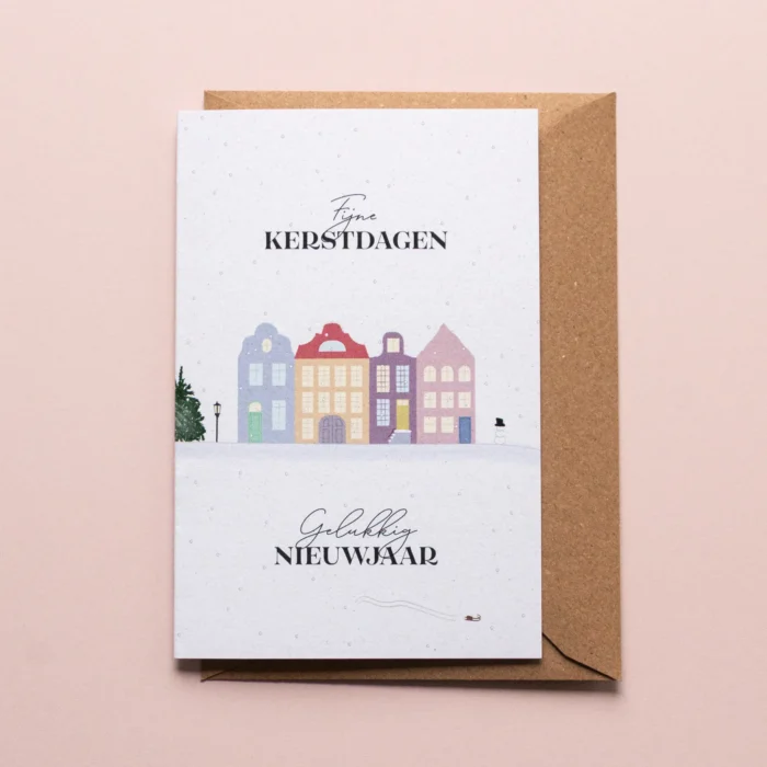 Kerstkaart Kleurrijk winterdorp met illustratie van huisjes in verschillende kleuren, een lantaarn, een grote kerstboom, een sneeuwman en op de voorgrond nog een klein sleetje. De illustratie toont een winters landschap met dwarrelende sneeuw en de tekst: 'Fijne kerstdagen, gelukkig nieuwjaar'.