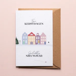 Kerstkaart Kleurrijk winterdorp met illustratie van huisjes in verschillende kleuren, een lantaarn, een grote kerstboom, een sneeuwman en op de voorgrond nog een klein sleetje. De illustratie toont een winters landschap met dwarrelende sneeuw en de tekst: 'Fijne kerstdagen, gelukkig nieuwjaar'.