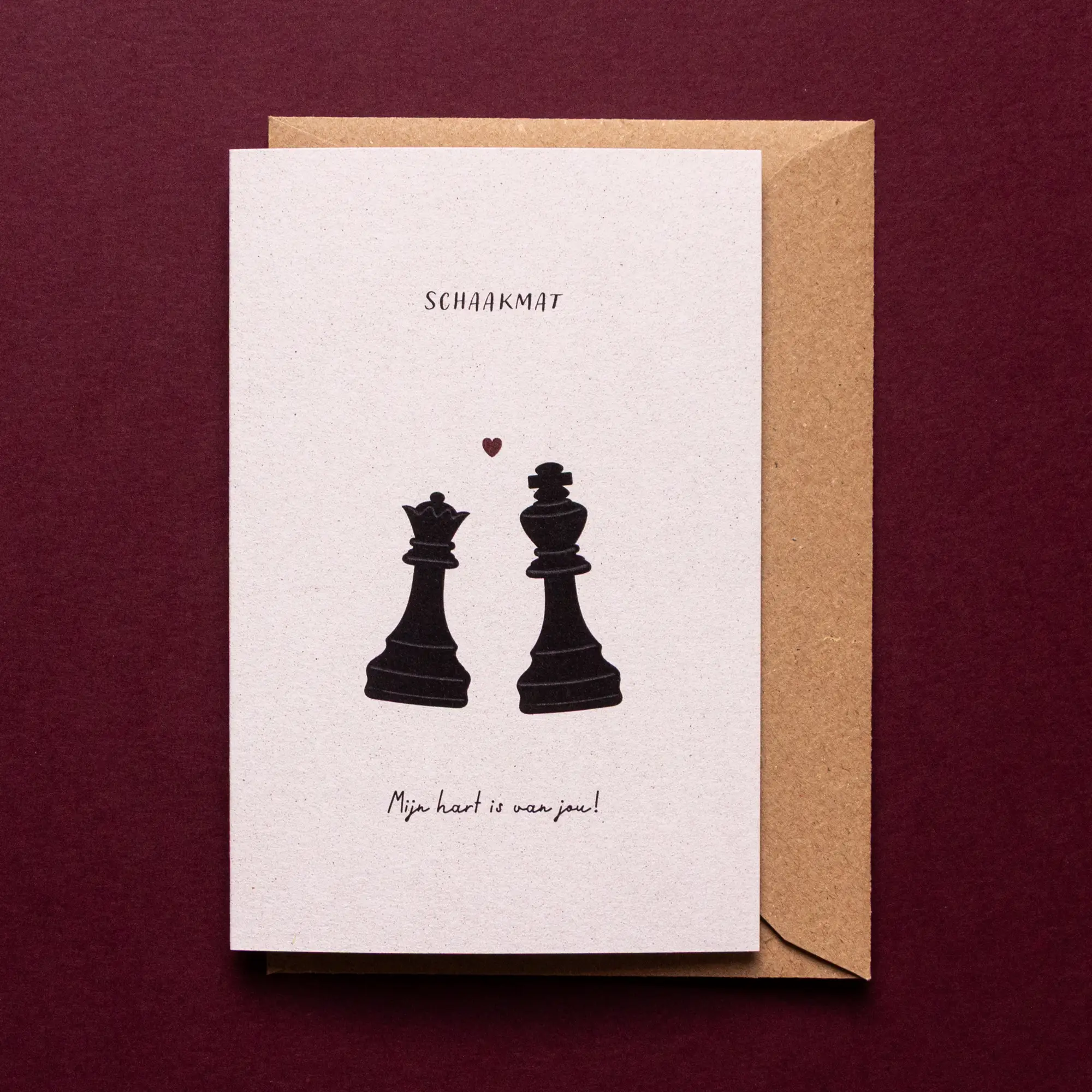 Romantische liefdeswenskaart Schaakmat met illustratie van een zwarte koning en koningin uit een schaakspel met een klein rood hartje en de tekst: 'Schaakmat, mijn hart is van jou!'.